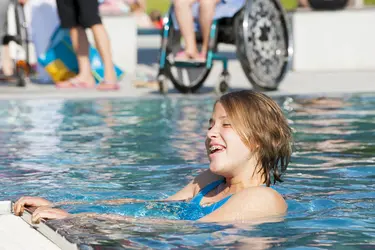 Mädchen im Schwimmbecken mit Rollstuhl am Beckenrand